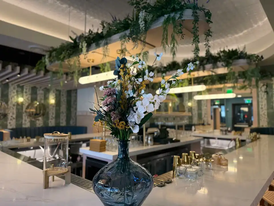 Bar centerpiece in a smoked glass vase beneath suspended greenery and wisteria installations