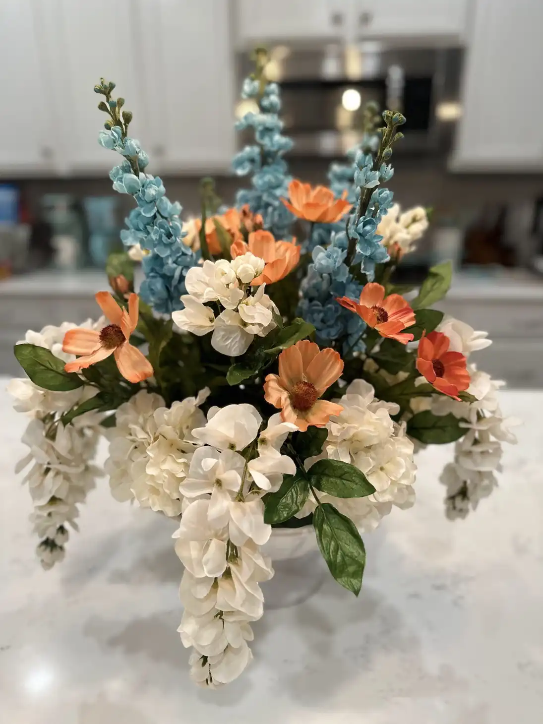 Tall arrangement of white hydrangea, peach blooms and dusty blue delphinium on a kitchen island
