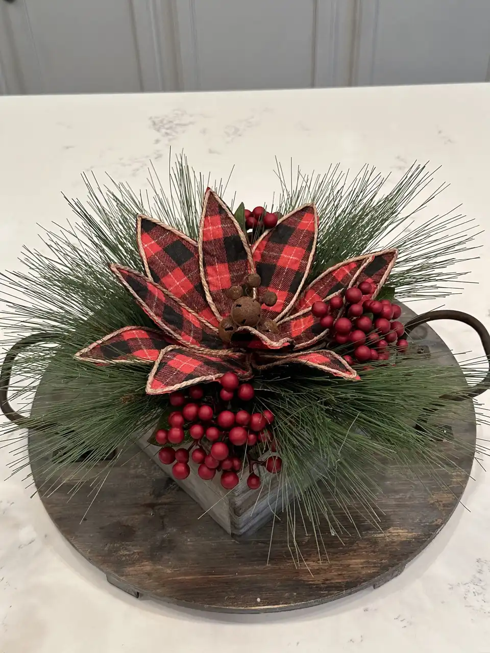 Buffalo plaid poinsettia centerpiece with red berries and pine on a wooden tray