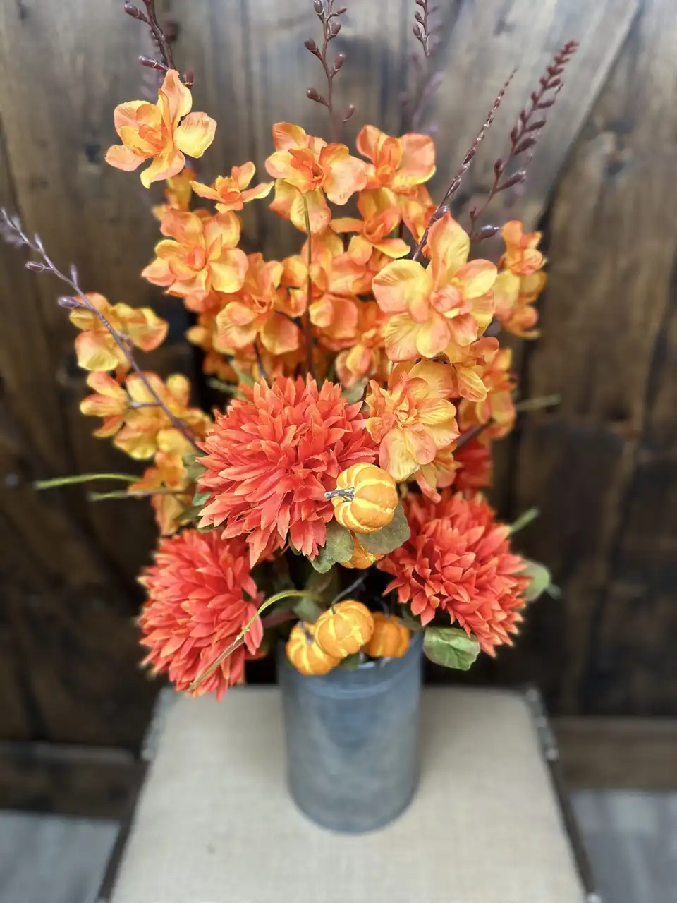 Bright orange orchids, dahlias and mini pumpkins in a tin vase