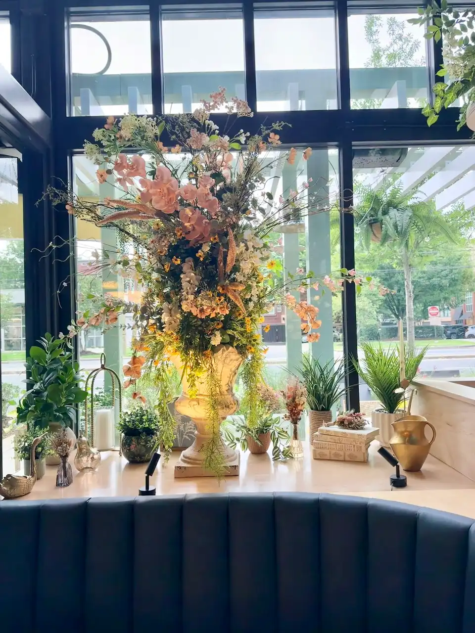 Large artificial floral arrangement in a pedestal urn behind a navy restaurant banquette