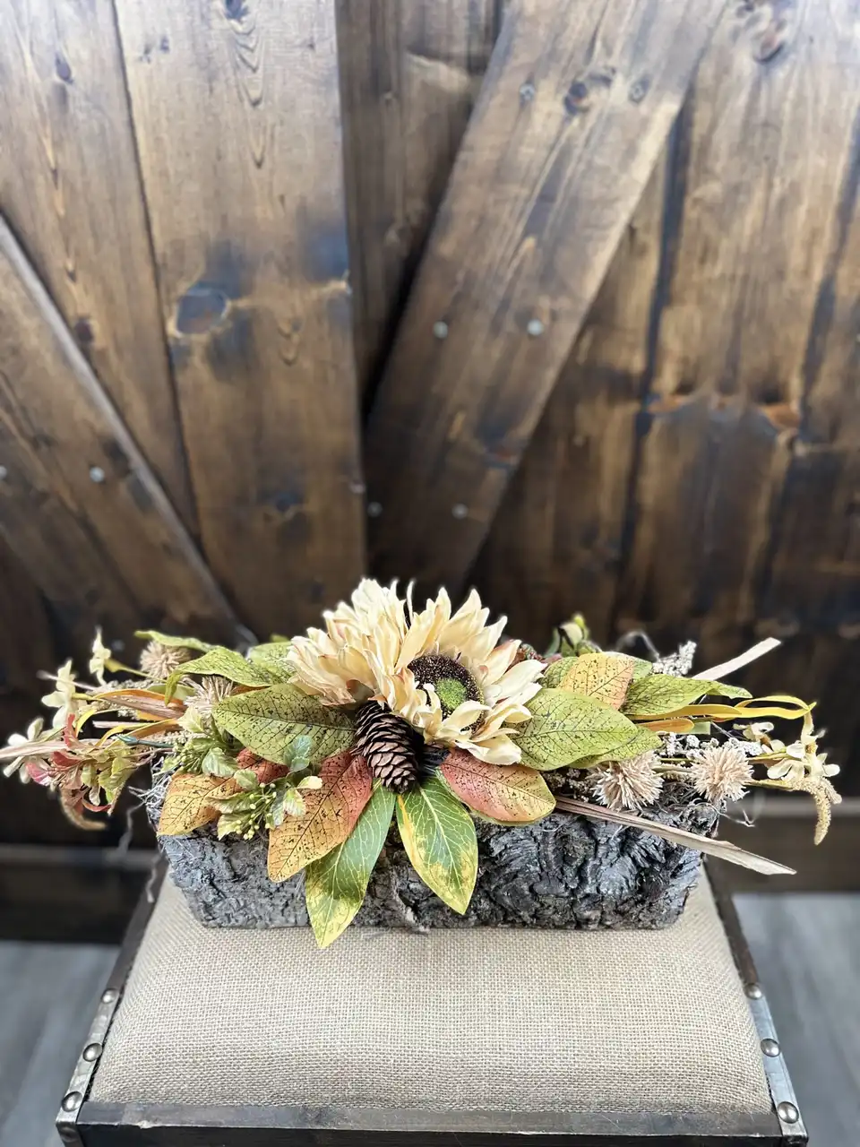 Long low table runner of faux sunflowers, pinecones and wheat in a bark planter