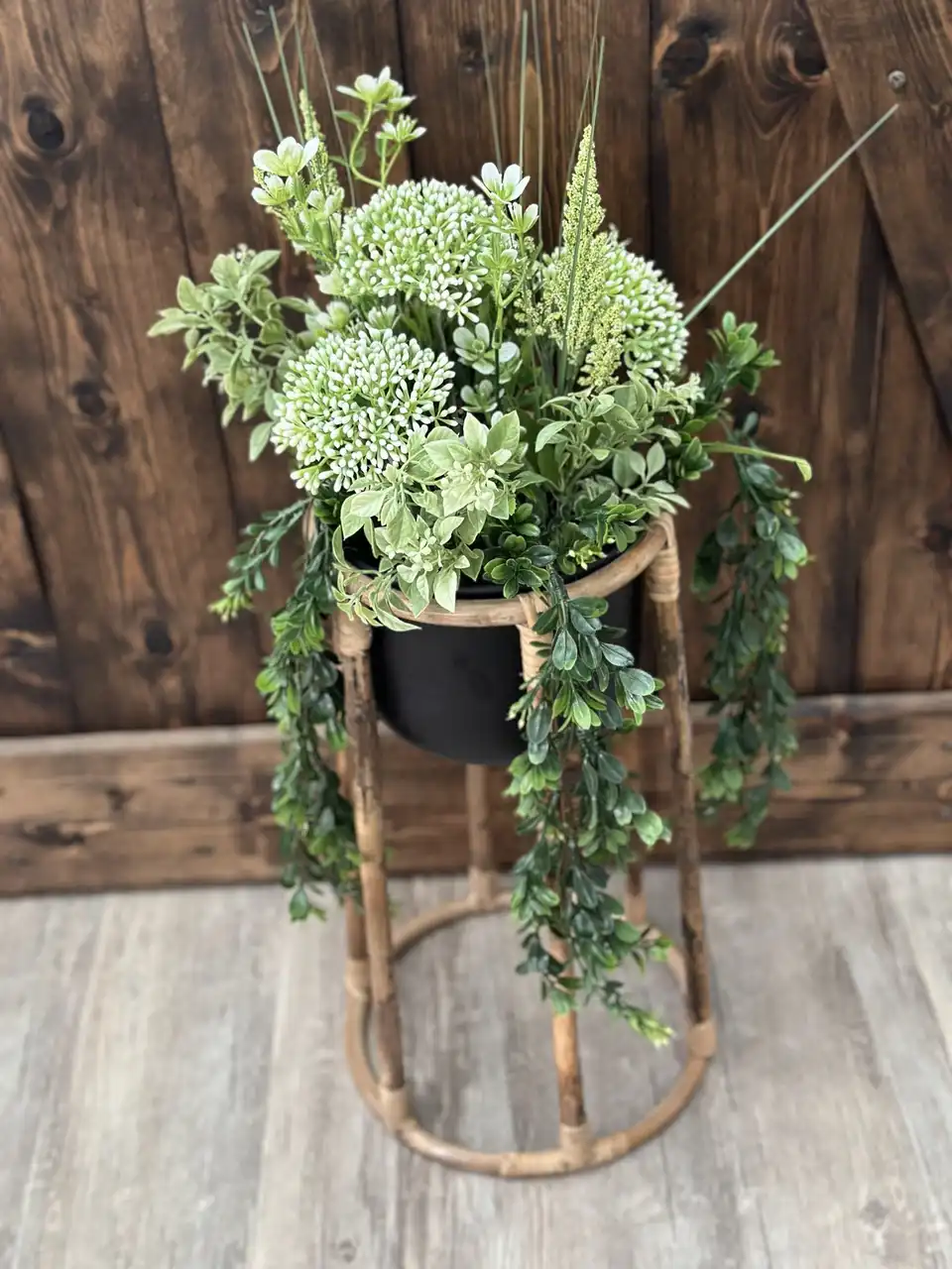 Trailing faux greenery and white blooms on a bamboo plant stand