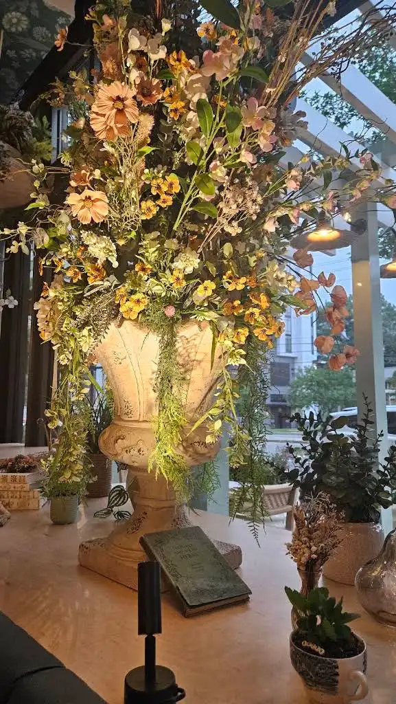 Peach and marigold faux flowers spilling from a stone urn on a restaurant window ledge with vintage books